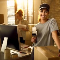 happy-courier-using-tape-dispenser-while-packing-boxes-delivery-looking-camera_637285-6605